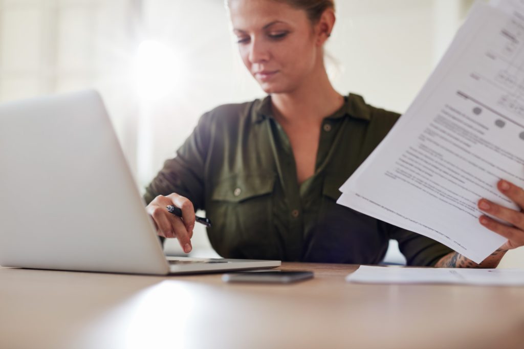 Young woman with documents working on laptop